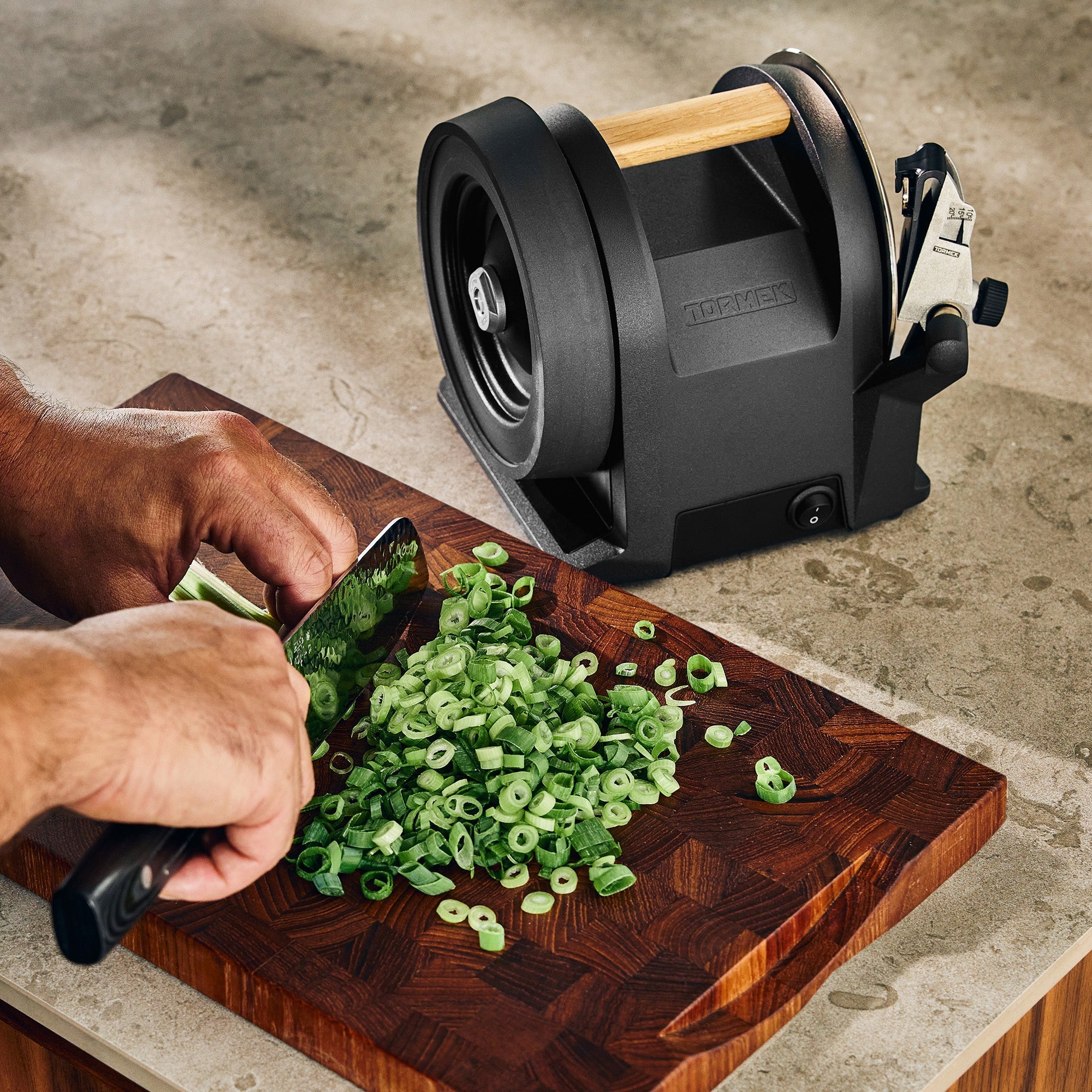 The Tormek T-1 Carbon Black on a stone counter with a person cutting leeks on a cutting board.