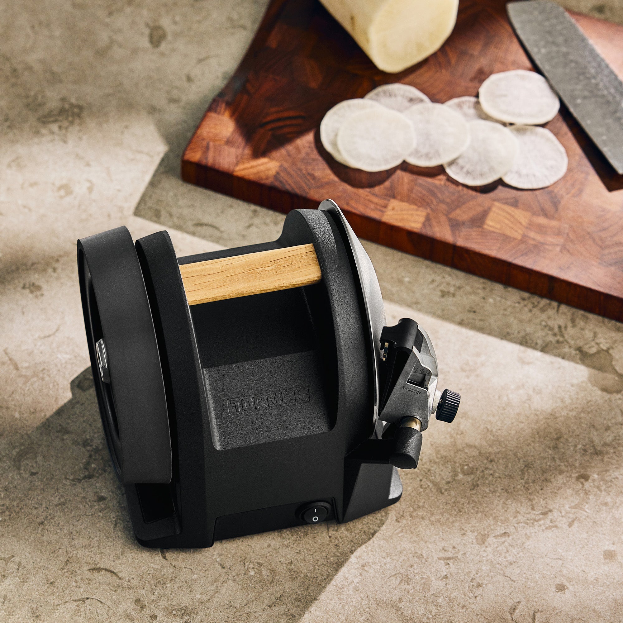A Tormek T-1 Carbon Black on a stone counter before a cutting board with radish on it