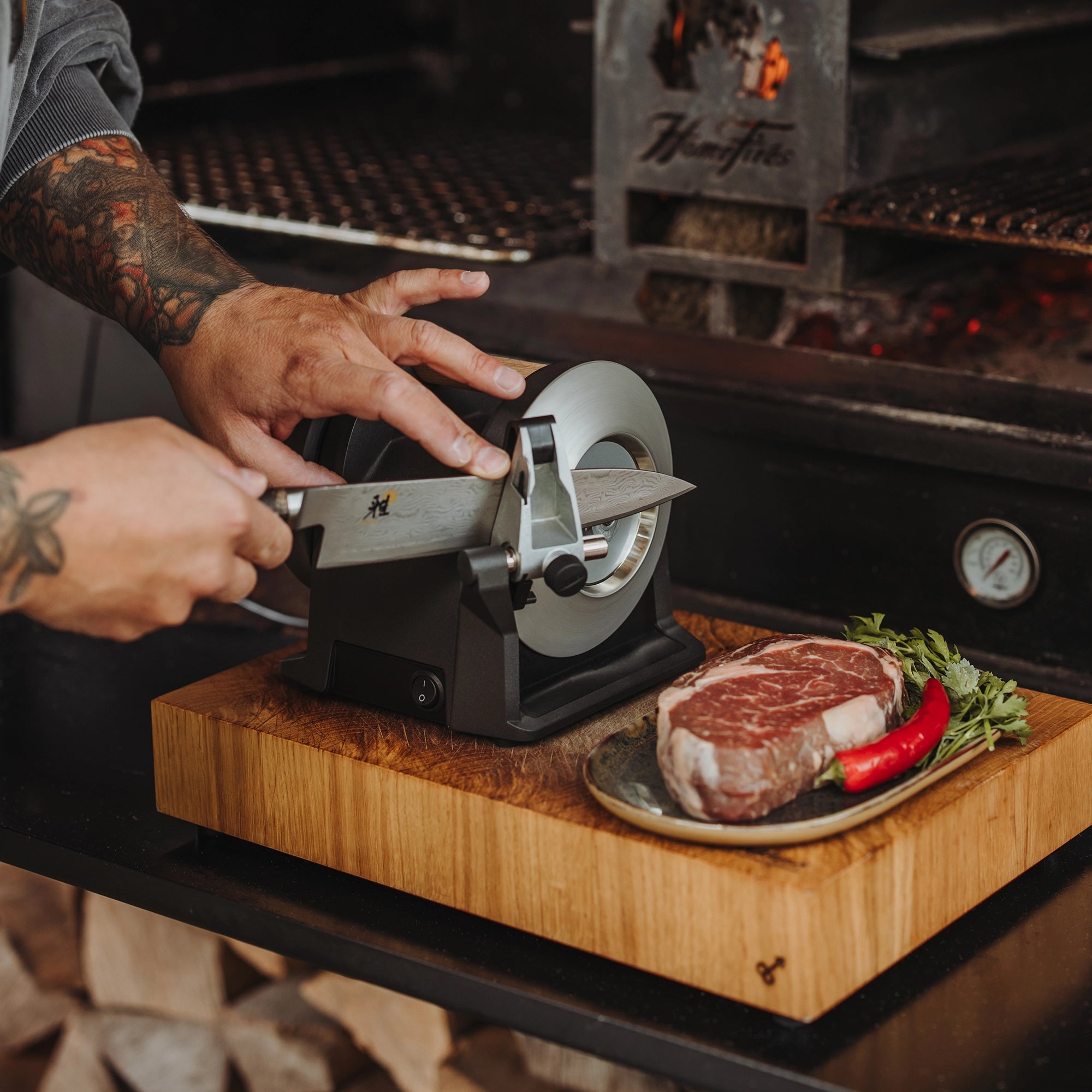 A knife is sharpened on the Tormek T-1 Carbon Black next to a grill.