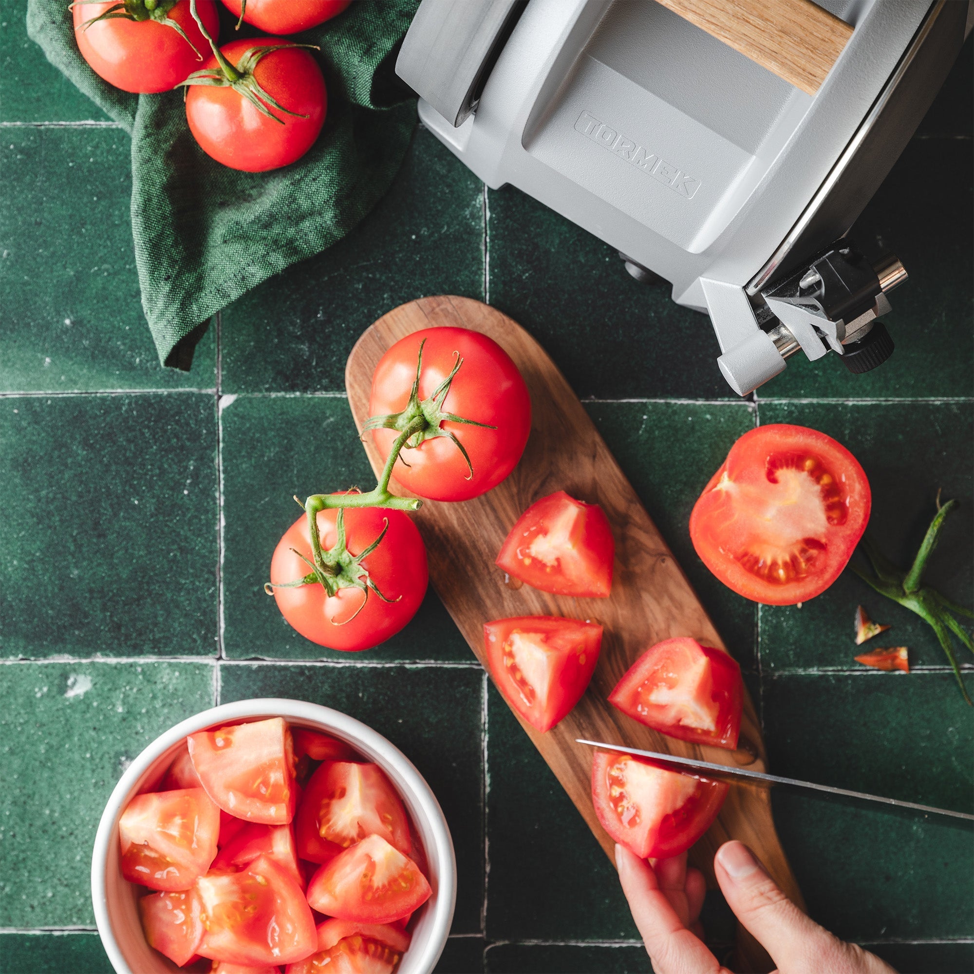 A person cutting tomatos on a cutting board and in the top corner is a Tormek T-1 Zinc Gray